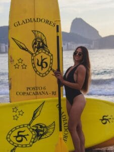 Mulher em pé na prancha de SUP ao lado das ondas suaves de Copacabana