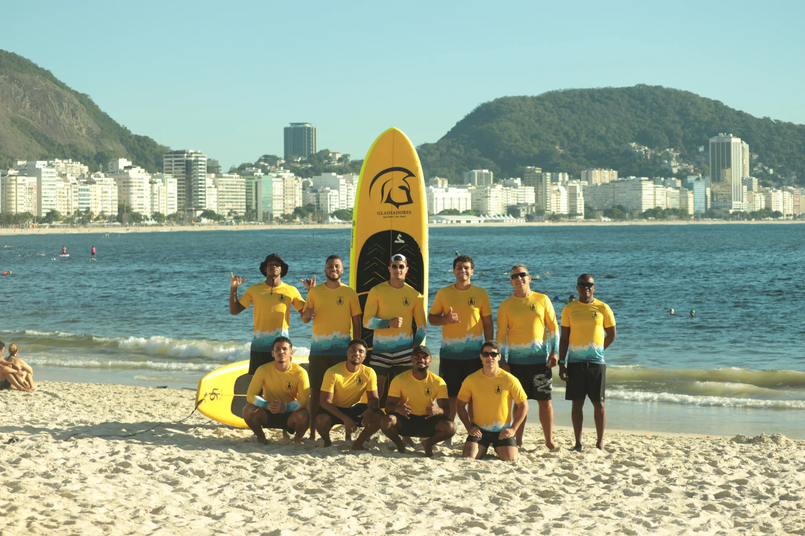 Equipe Gladiadores SUP reunida na praia de Copacabana com prancha e uniforme, prática de stand up paddle Copacabana.
