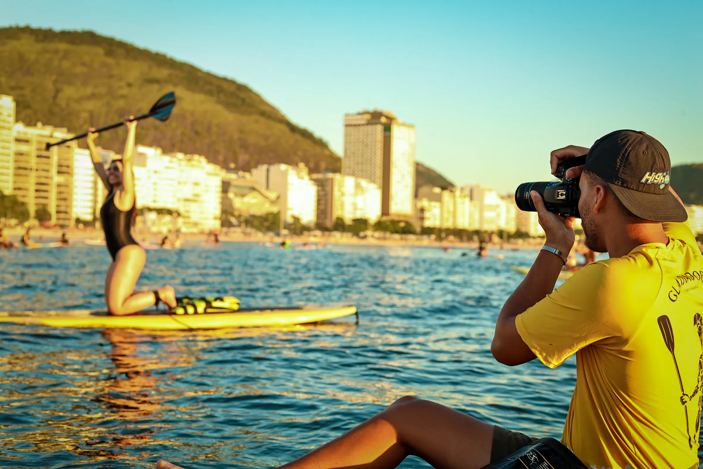 Fotógrafo profissional da Gladiadores SUP capturando uma mulher praticando stand up paddle em Copacabana durante o pôr do sol.